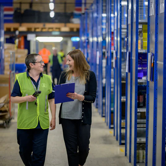Warehouse staff discussing inventory with clipboard in storage aisle, NZ packaging supplies