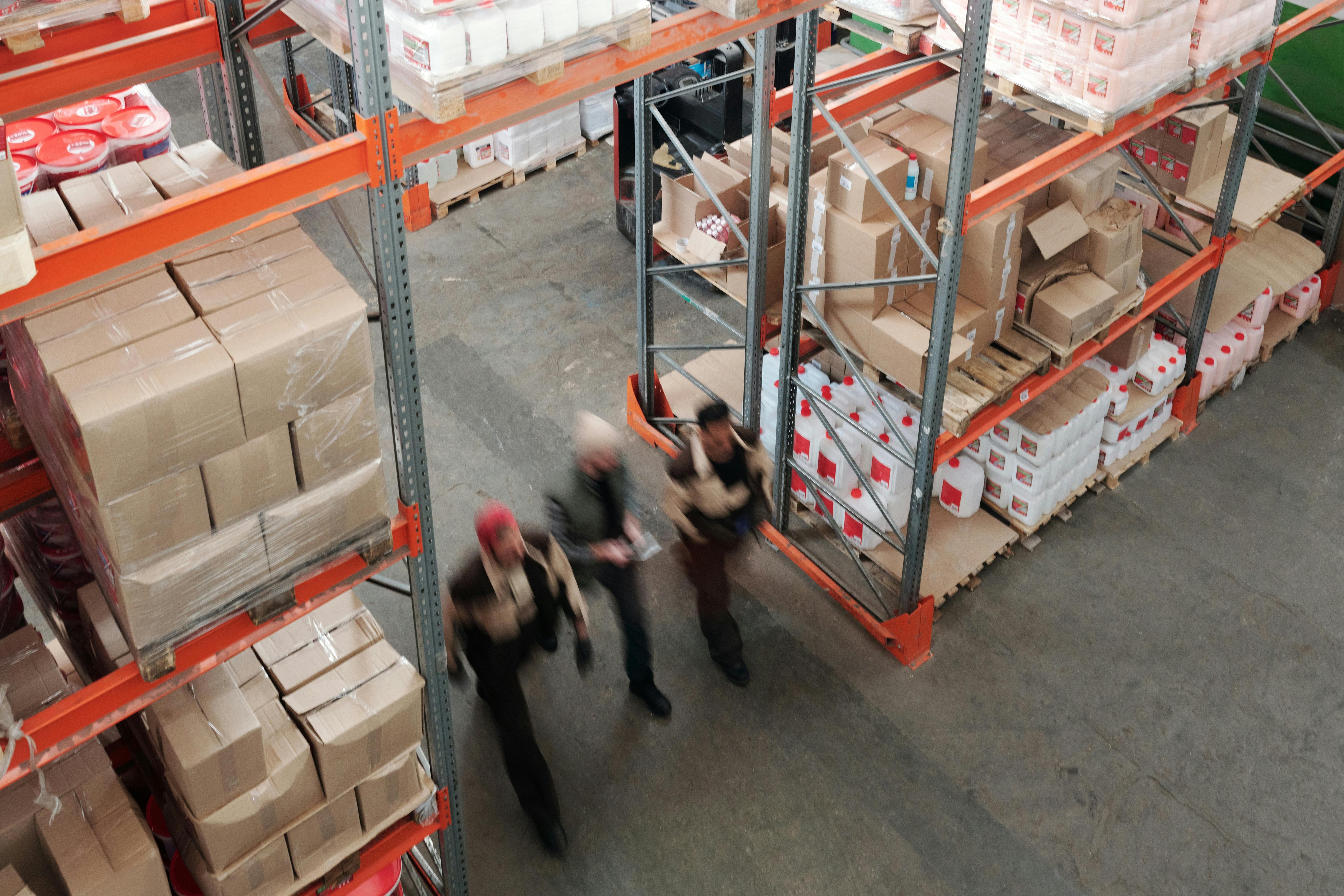 Warehouse staff moving boxes and supplies on pallets between industrial shelves